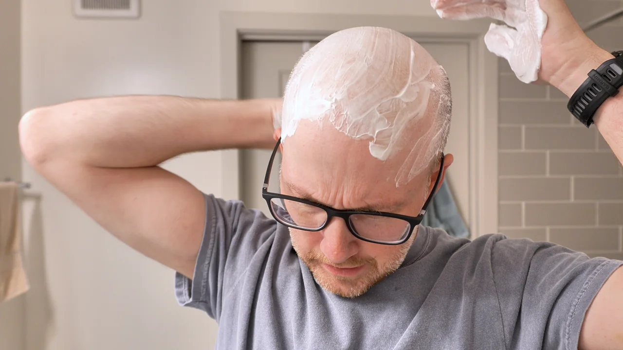 Shawn spreading shaving cream over the top and back of his head with both hands