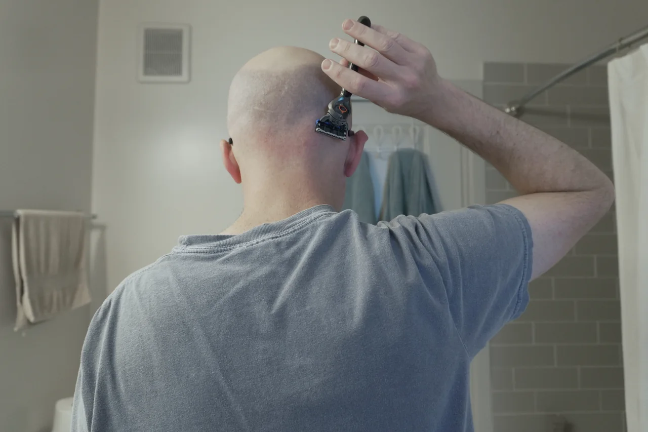 Rear view of Shawn positioning a cartridge razor on the back of his head