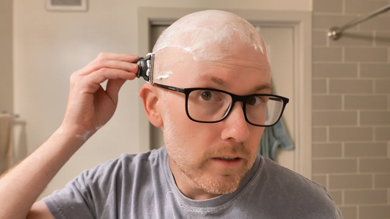 Shawn using a cartridge razor on the side of his lathered head above the ear