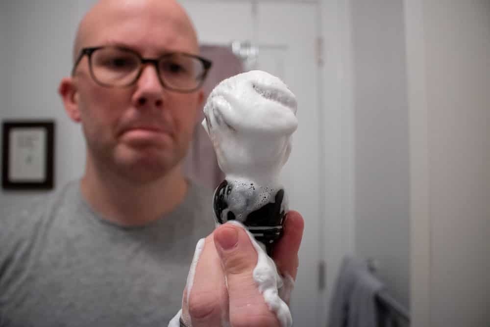 man holding loaded shaving brush close to camera