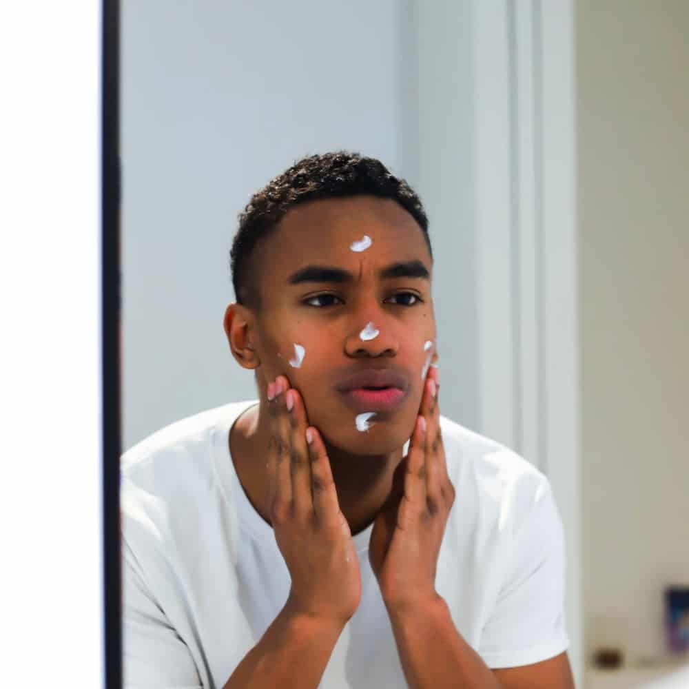 man applying face cream in mirror
