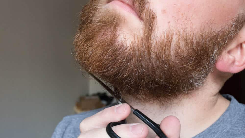 alternate angle of man trimming facial hair on chin