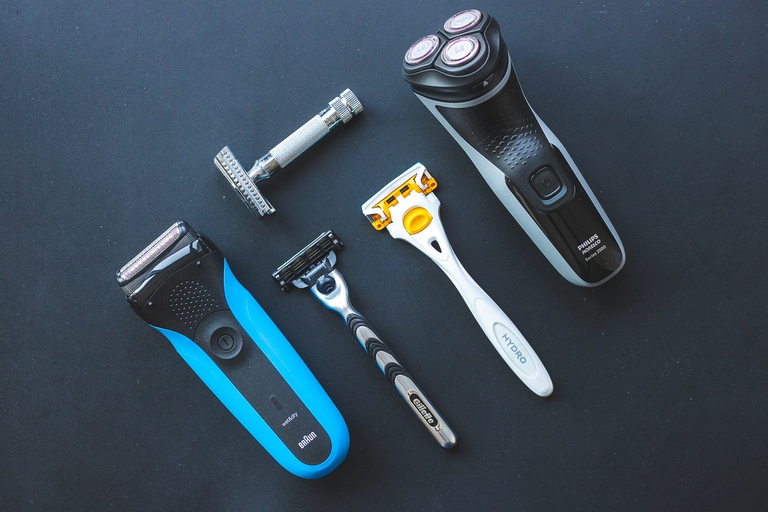assorted electric shavers and cartridge razors on a black mat