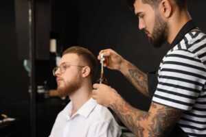 barber holding an amber bottle and dropper client in background