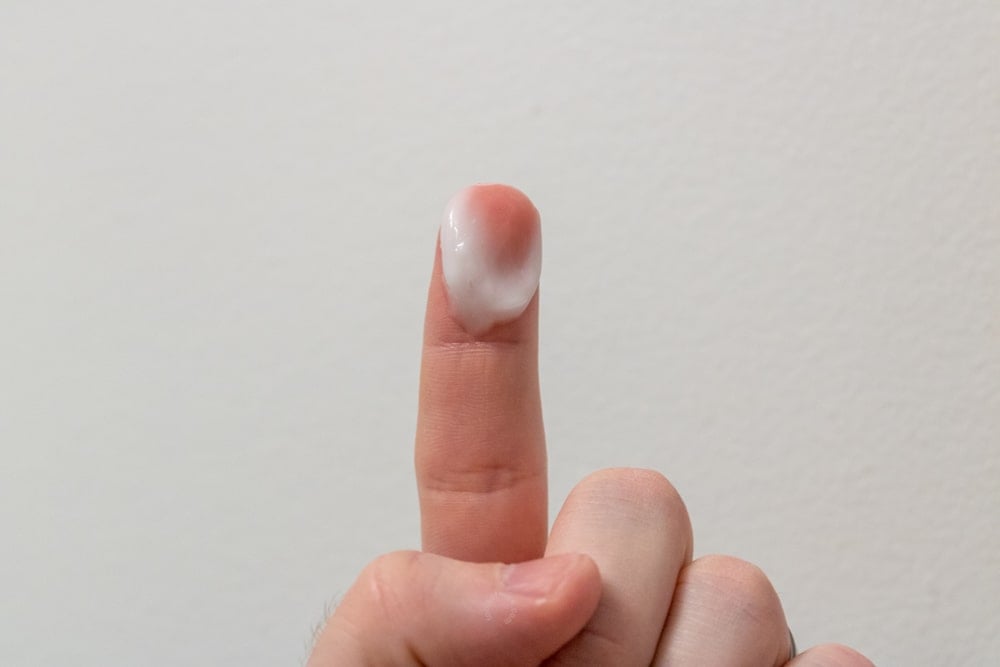 fingertip holding up face cream to demonstrate thickness