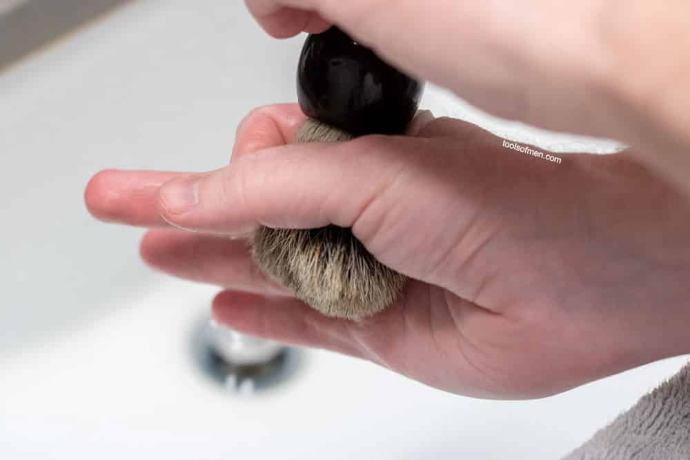 hand squeezing shaving brush water dripping out