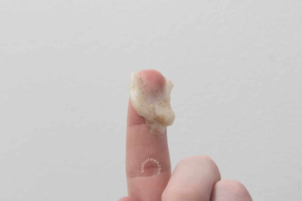 holding the face scrub on fingertip to demonstrate thickness