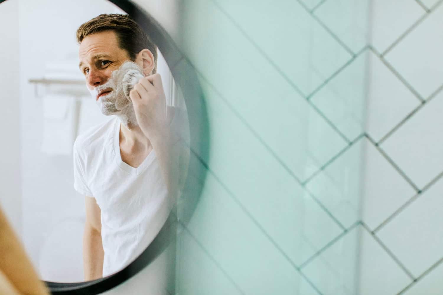 man applying shave cream with a shave brush in front of mirror