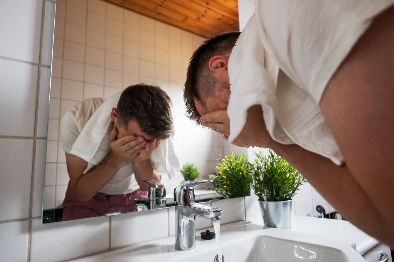 man bent over washign face over sink