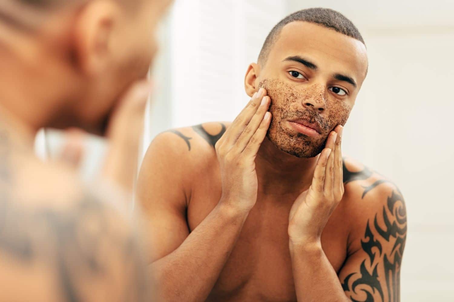man exfoliating face while looking into mirror