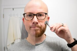 man half clean shaven and half beard holding razor to face
