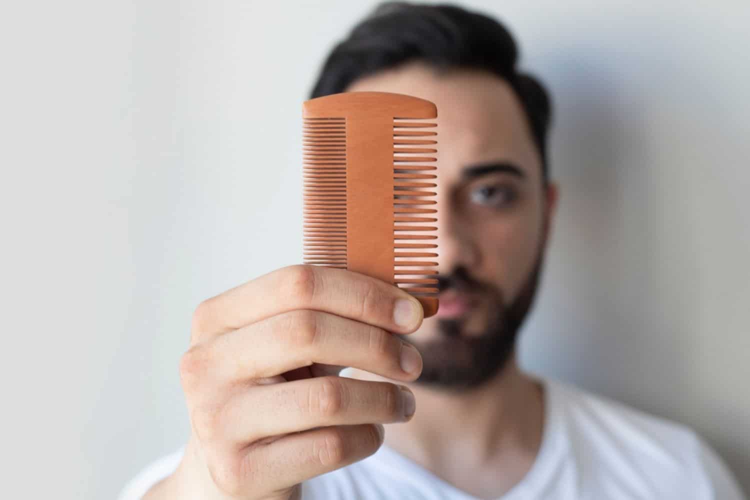 man holding up a wooden beard comb
