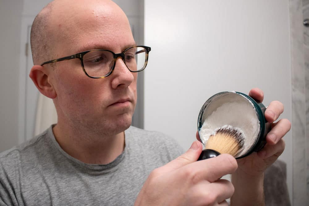 man holding up body shop shaving cream and using a shaving brush to scoop out cream