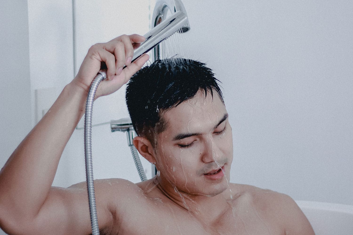 man in bathtub holding a shower
