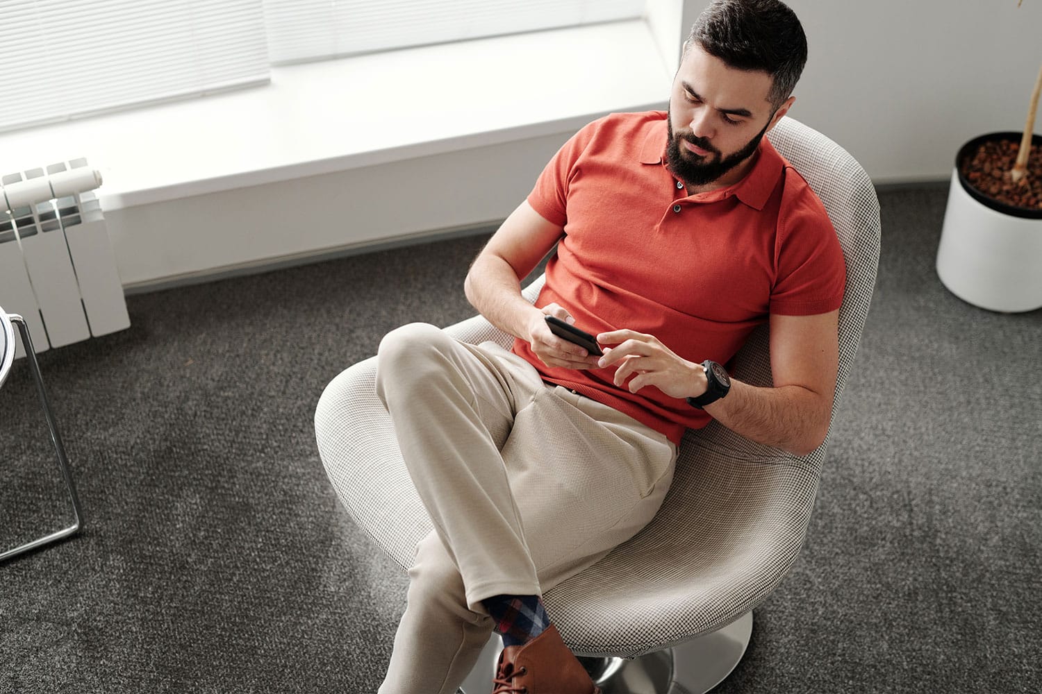 man in red polo shirt sitting while using a cellphone