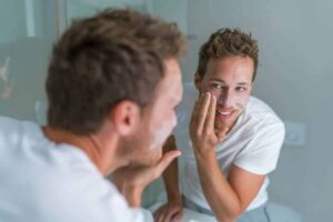 man moisturizing face while smiling in mirror
