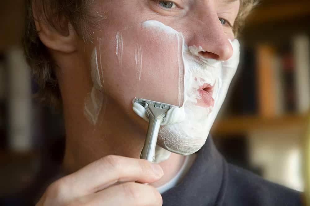 man shaving cheeks with razor