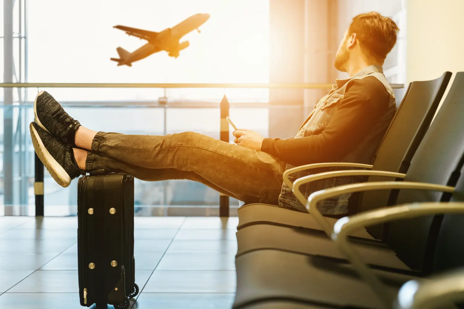 man sitting in airport with feet on luggage