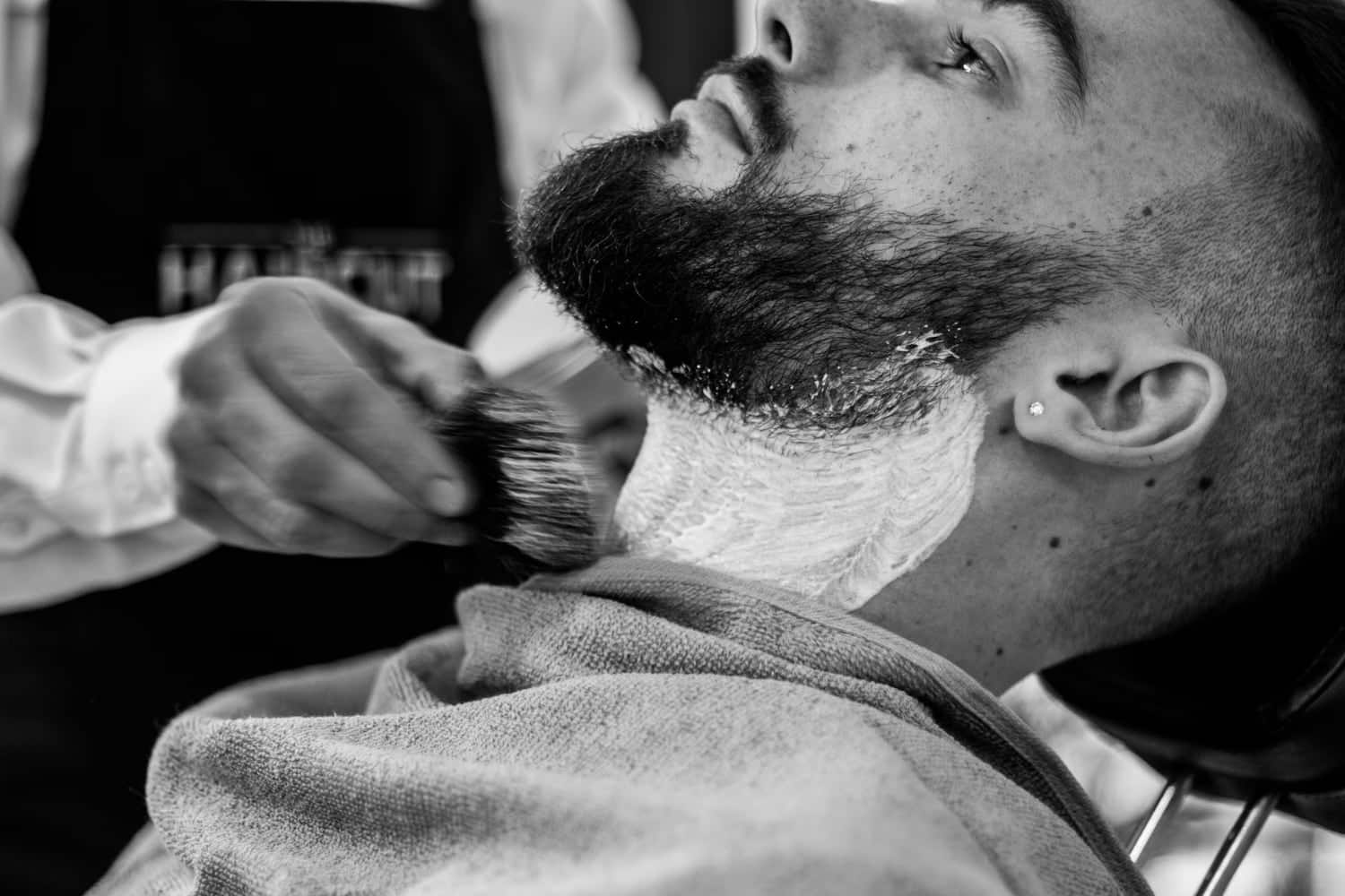 man sitting in barber chair with shaving cream applied to neck