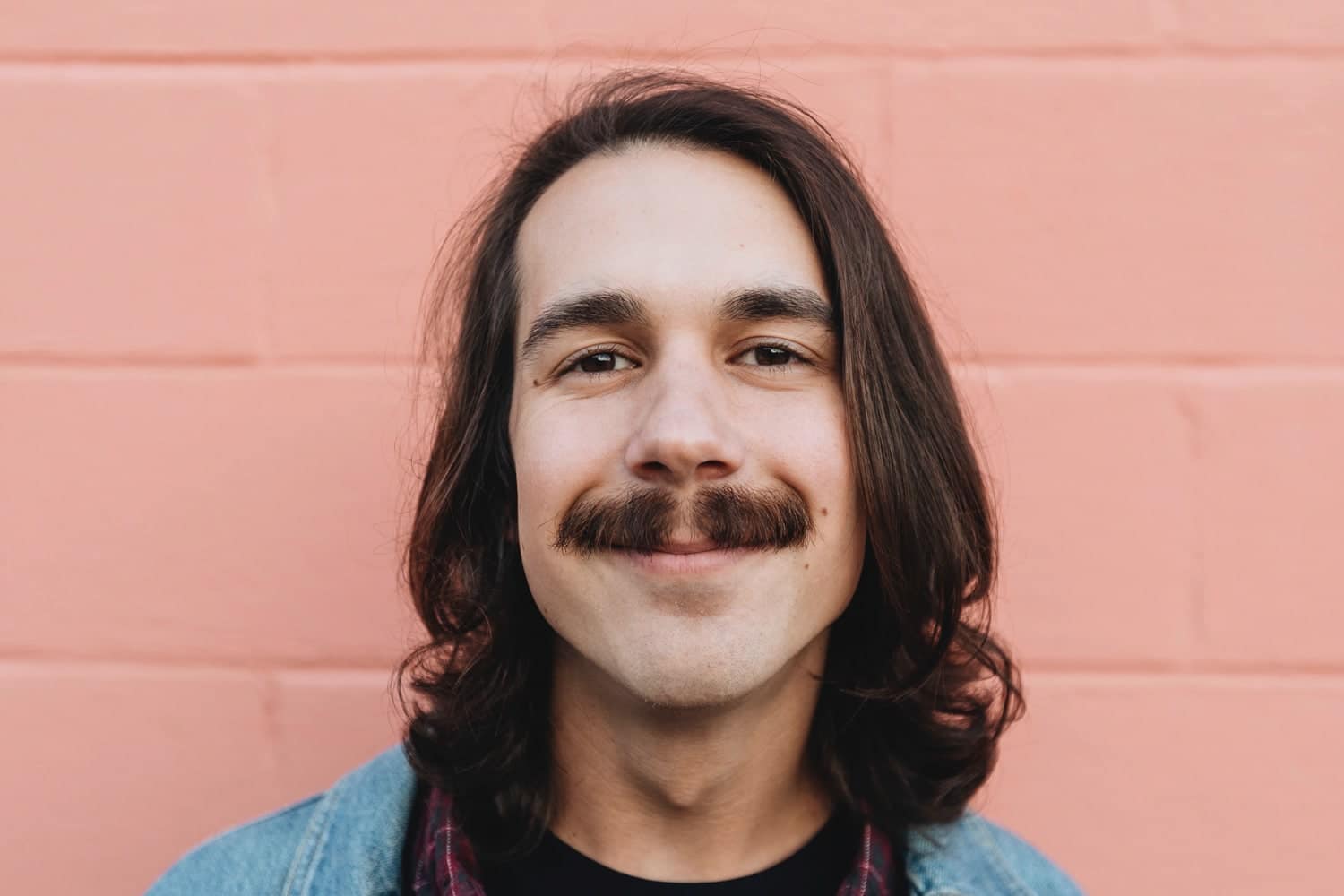 man smiling with long hair and a thick mustache