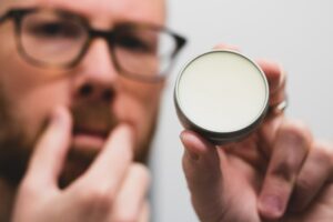 man stroking mustache while holding a tin of wax