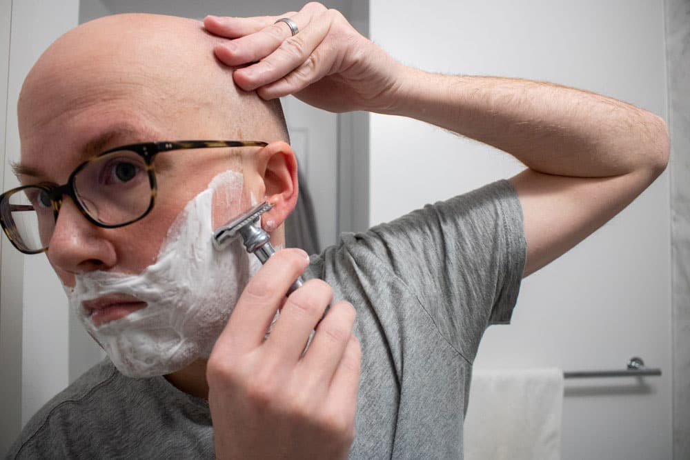 man using a safety razor on face with cella shaving cream applied 1