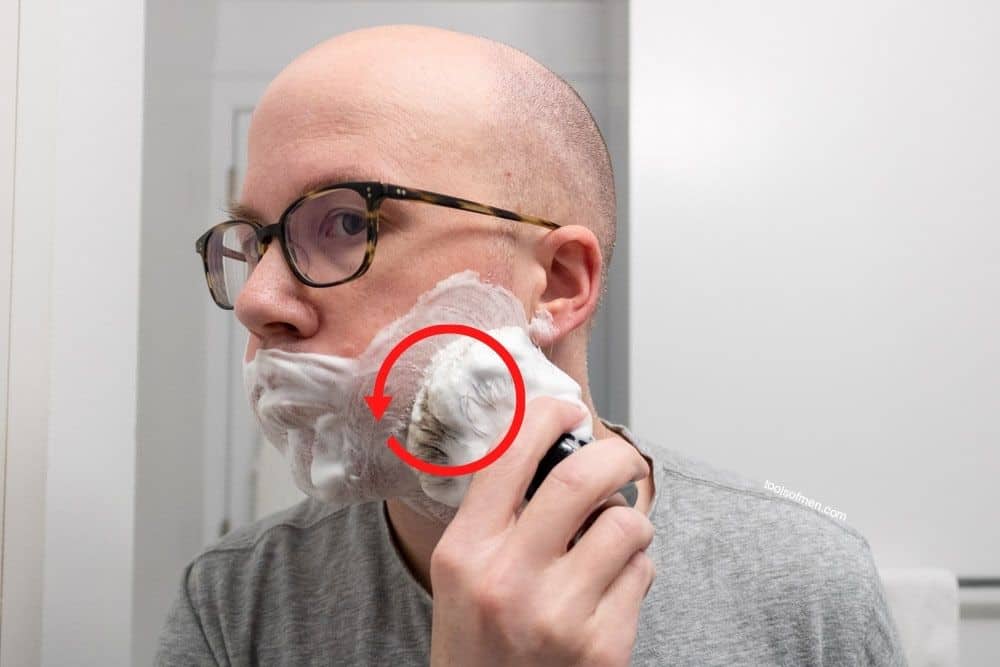 man using shaving brush to apply cream red circular arrow demonstrating direction