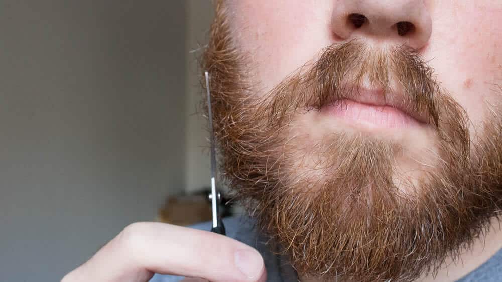 man using shears on cheek to trim beard
