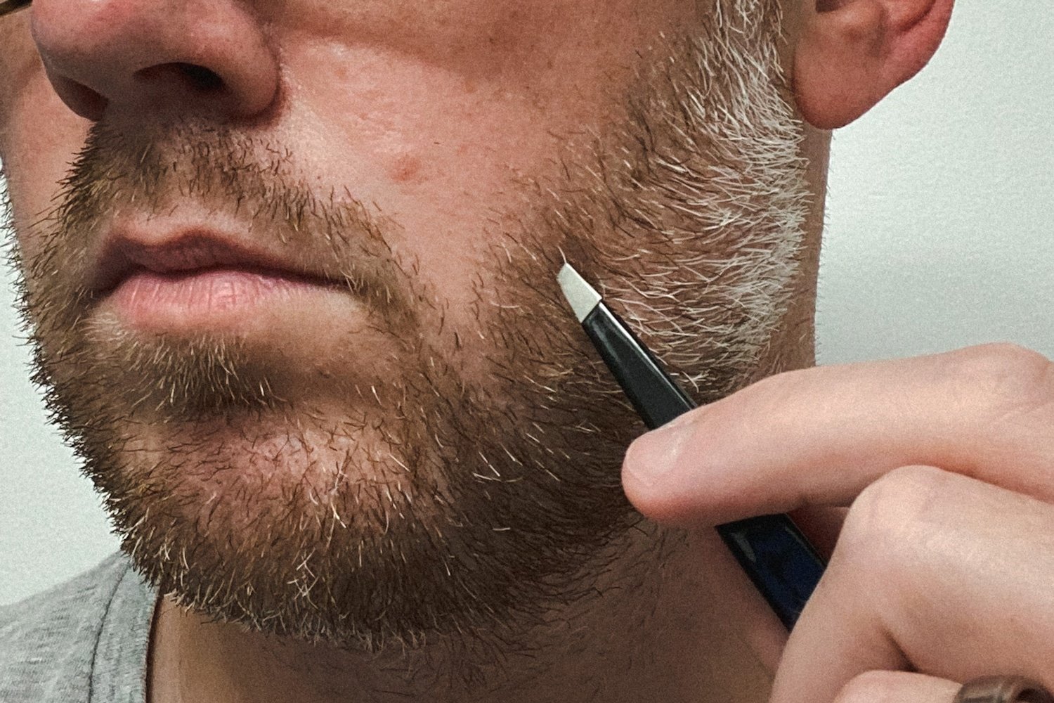 man using tweezers on beard