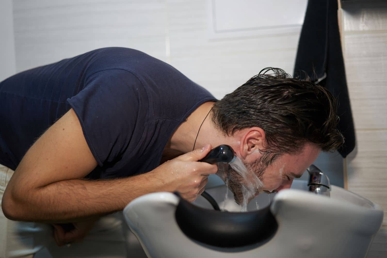 man washing his beard with a handheld spray over sink