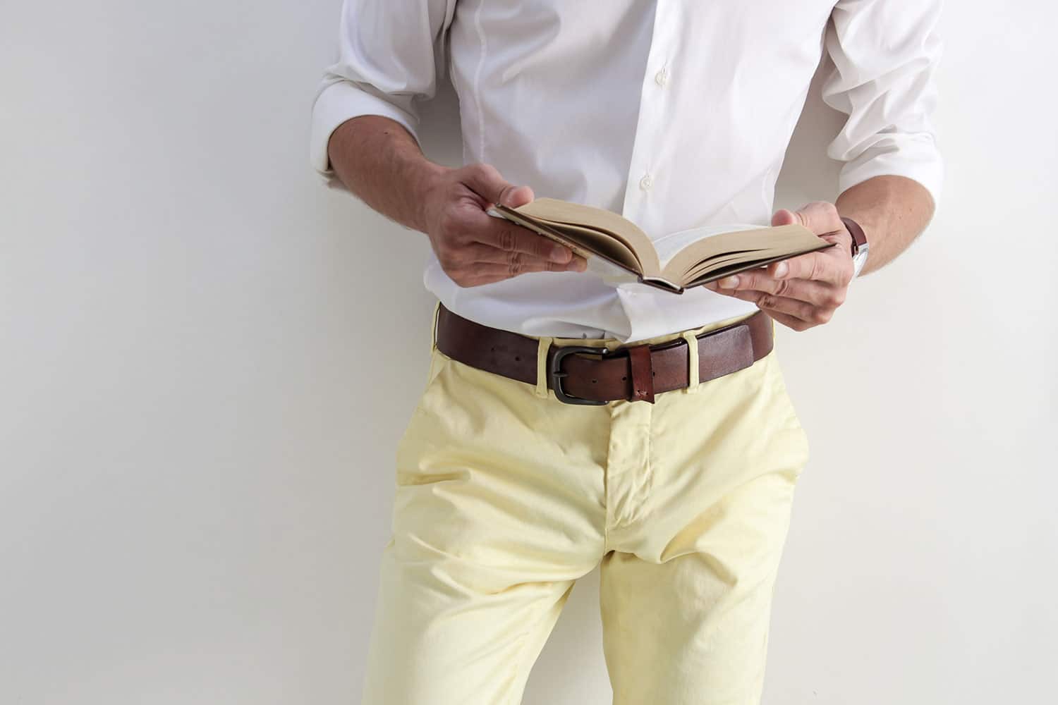 man wearing leather belt leaning on the wall while reading book