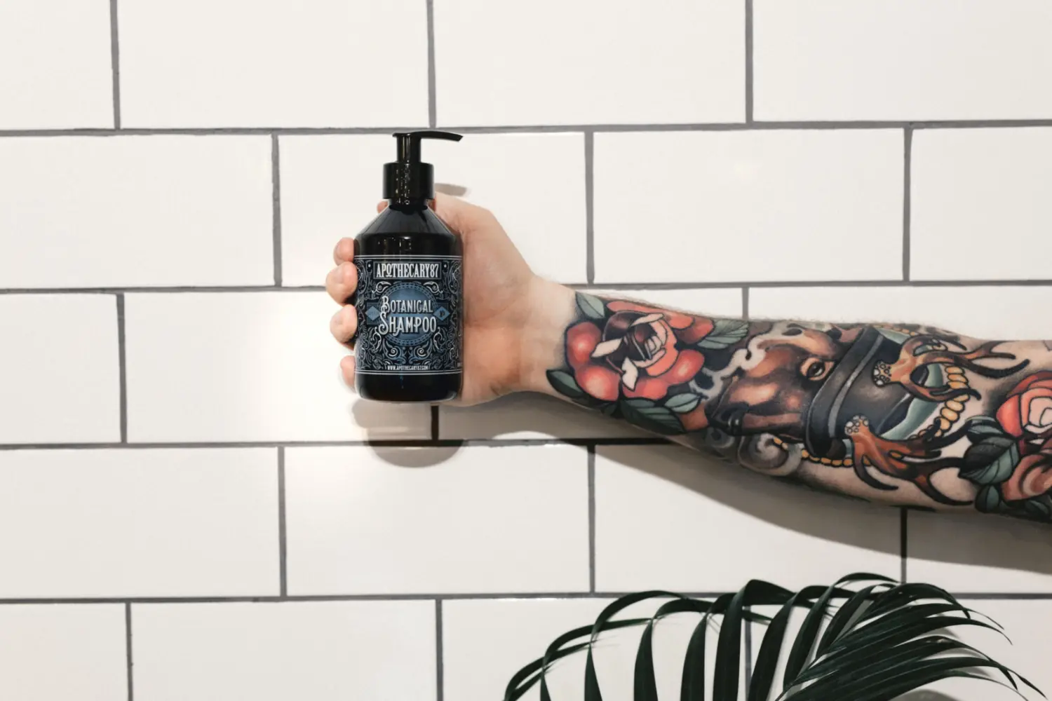 man with tattoo arm holding shampoo bottle