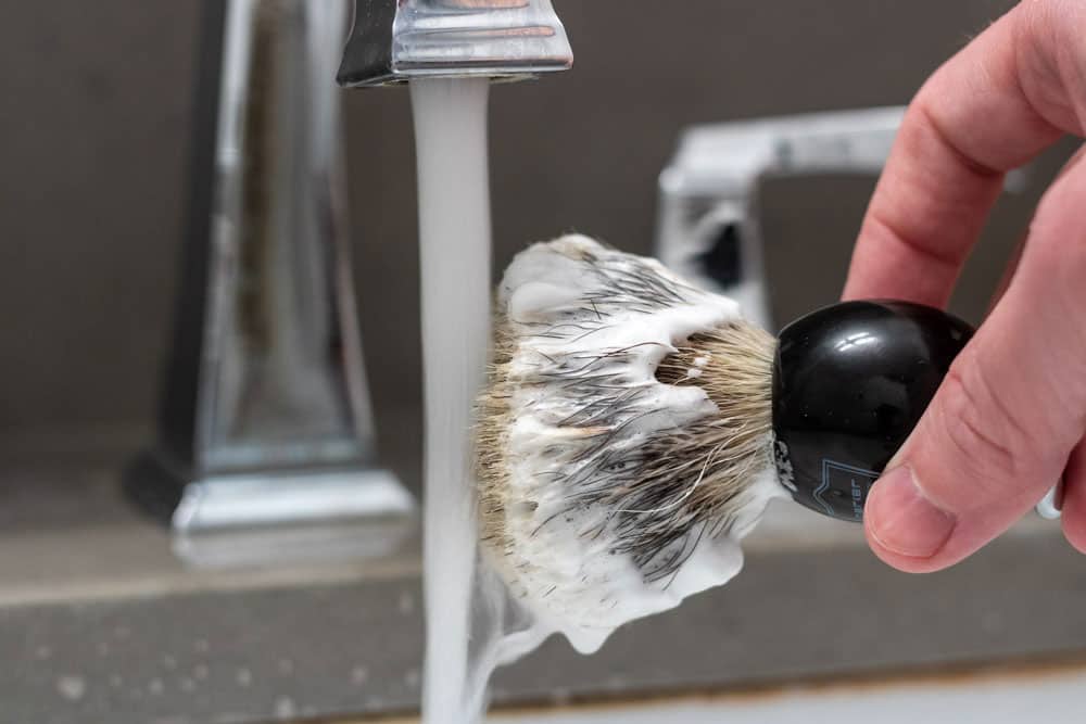 shaving brush slightly held under bathroom faucet