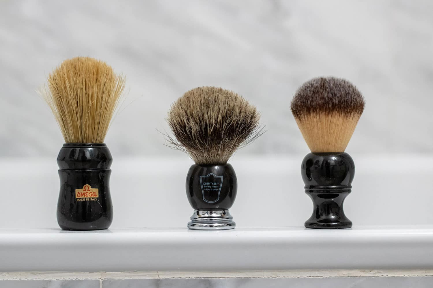 three different shaving brushes on bathtub ledge