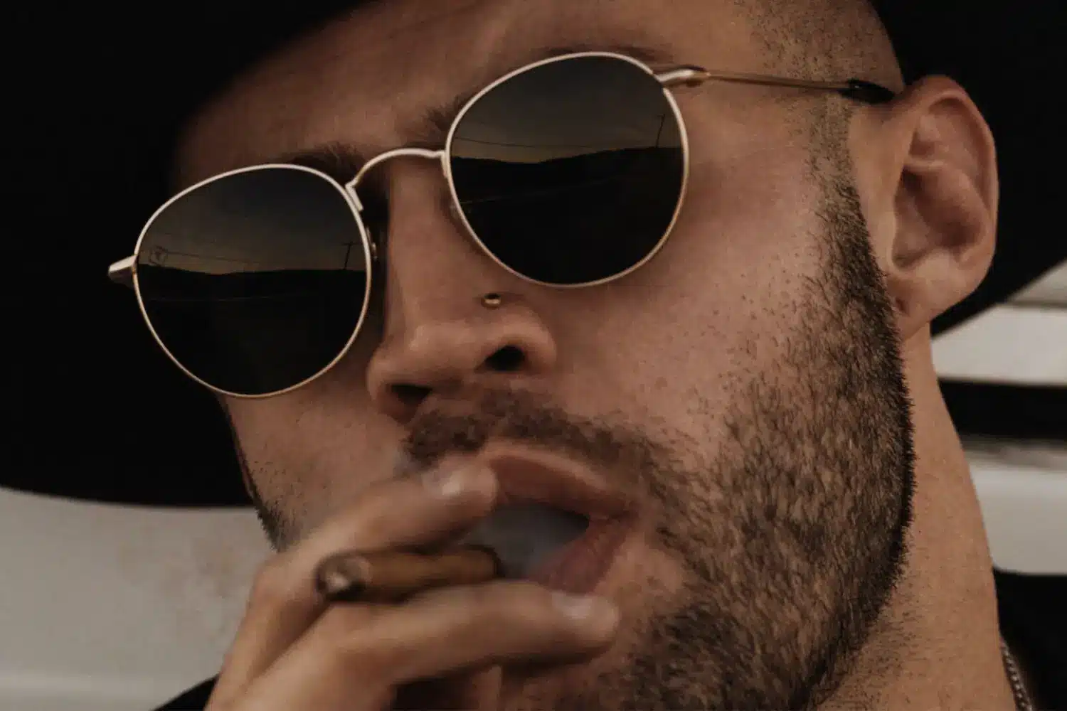 man with sunglasses and pierced nose smoking cigar